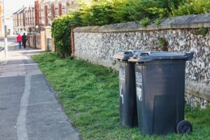 Wheeled trash bins on pavement outside of house waiting for garbage collection