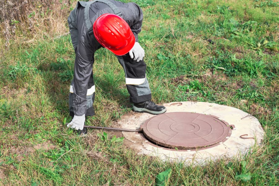 Worker in red helmet opening manhole with crowbar