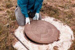 Worker lifts manhole cover for septic system inspection