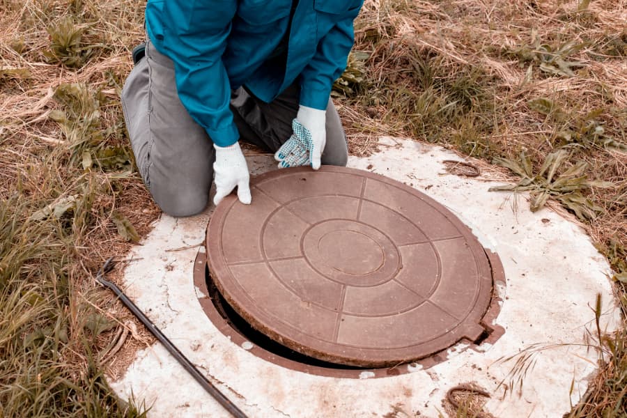 Worker lifts manhole cover for septic system inspection